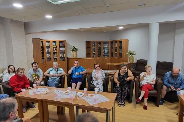 Mieszkańcy siedzą w fotelach w kawiarence i odpowiadaja na pytania quizu.