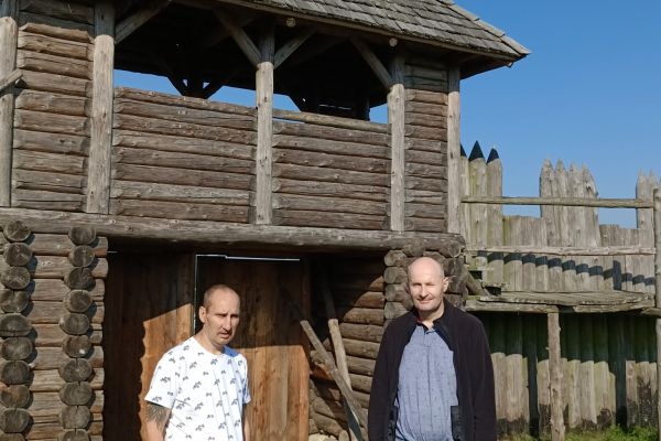 Zdjęcie dwuch mieszkańców przy osadzie drewnianej.