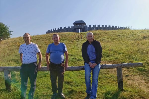 Mieszkańcy na polu z widokiem osady drewnianej.