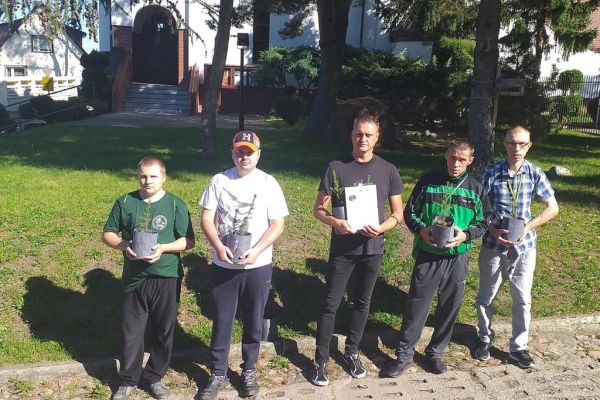Mieszkańcy wraz z opiekunem z podziękowaniami stoją do zdjęcia grupowego po sprzątaniu lasu.