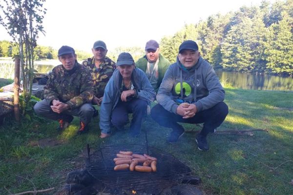 Mieszkańcy przy jeziorze smarza kiełbaski na grillu.