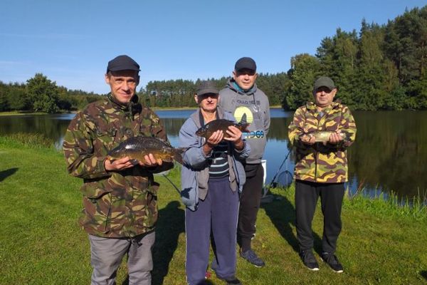 Grupowe zdjęcie mieszkańców nad jeziorem ze złowionymi rybami.