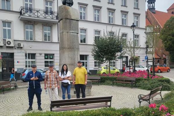 Czworo mieszkańców zwiedza stare miasto Grudziądz przy pomniku.