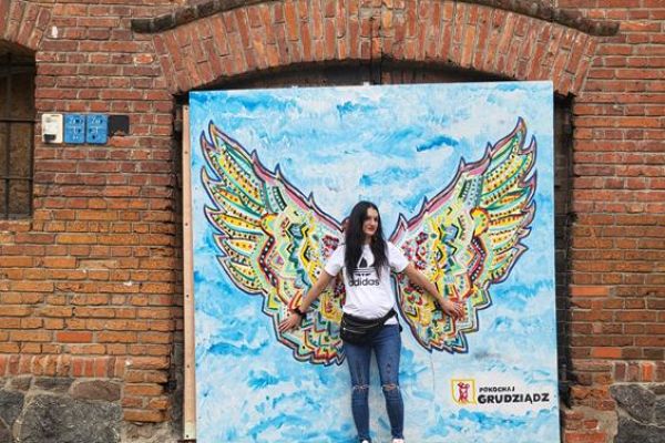 Mieszkanka przy plakacie ze skrzydłami w Grudziądzu.