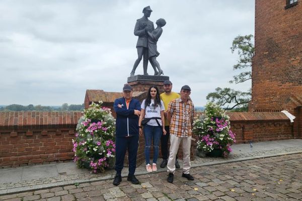 Czworo mieszkańców zwiedza stare miasto Grudziądz przy pomniku.