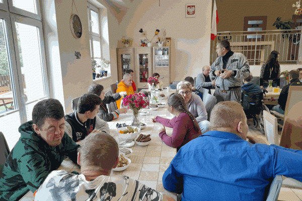 Mieszkańcy wraz z innymi uczestnikami projektu przy stolikach z poczęstunkiem.