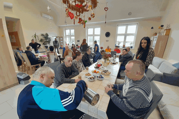 Mieszkańcy wraz z innymi uczestnikami projektu przy stolikach z poczęstunkiem.