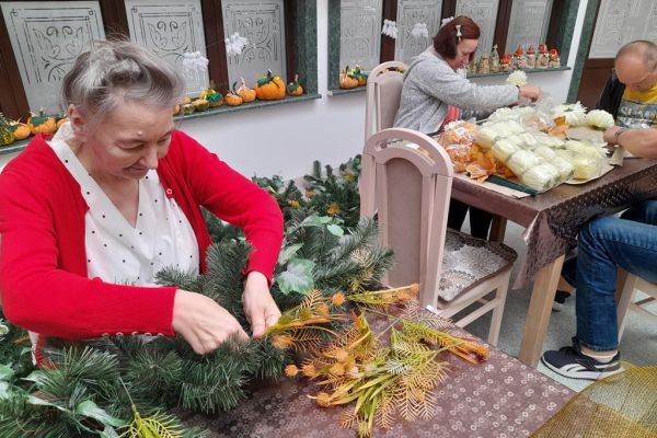 Mieszkańcy wykonują wiązanki na cmętarz siedząc przy stolikach.