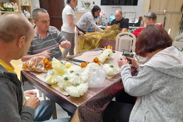 Mieszkańcy wykonują wiązanki na cmętarz siedząc przy stolikach.