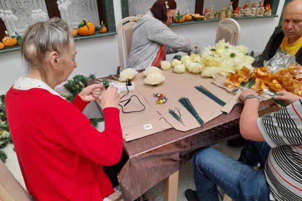 Mieszkańcy wykonują wiązanki na cmętarz siedząc przy stolikach.