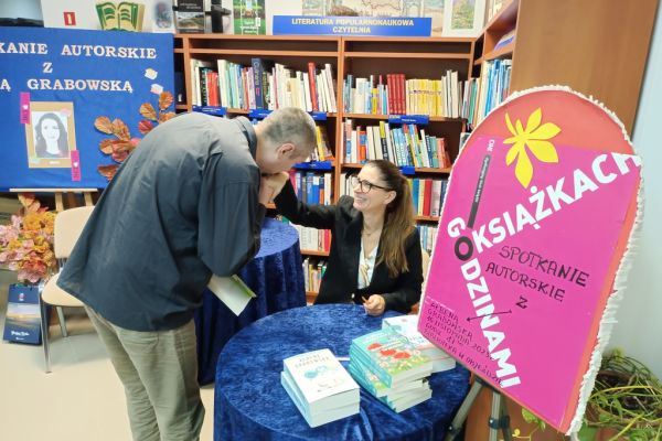 Mieszkaniec wita się z pisarką siedzącą na krześle całując w rękę.