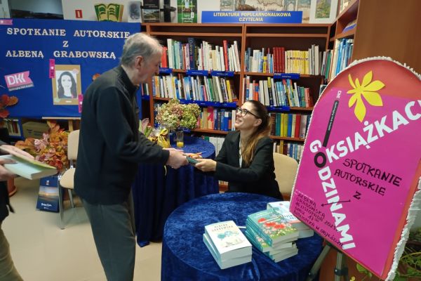 Mieszkaniec kupuje książkę od siedzącej pisarki.