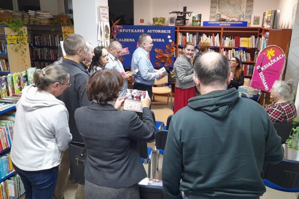 Mieszkańcy stoją w kolejce po autograf do siedzącej pisarki.