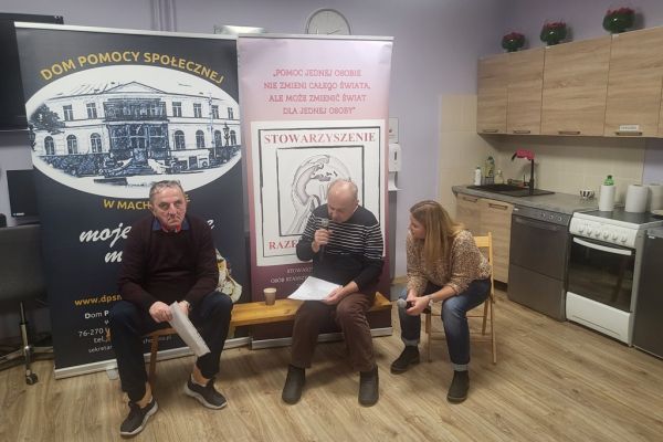 Dwoje mieszkańców siedzi i ćwiczy śpiew przy instruktorce warsztatów.