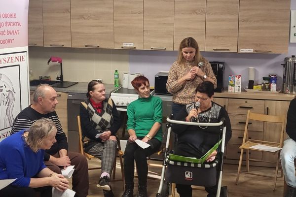 Mieszkanka DPS w Lubuczewie na siedząco śpiewa piosenkę wśród innych uczestników warsztatów.