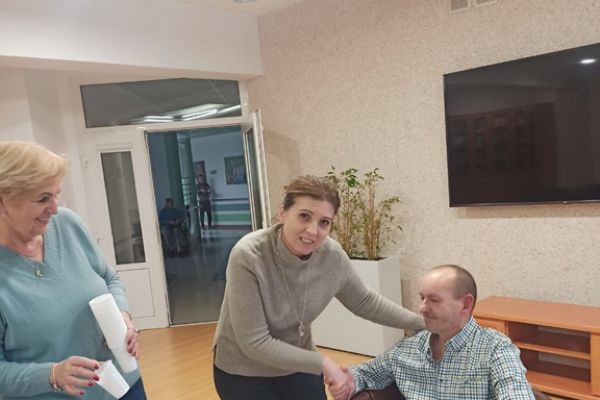 ieszkaniec siedzi a dwie pracownice składaja życzenia.