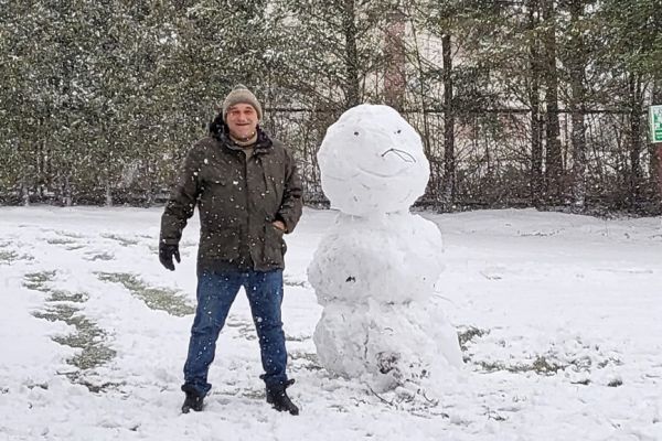 Mieszkaniec stoi przy ulepionym bałwanie.