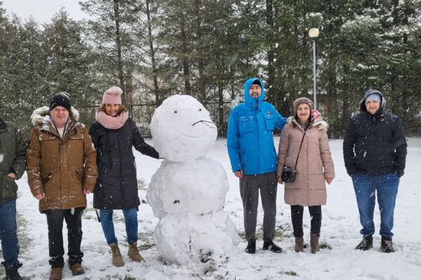 Mieszkańcy stoja przy ulepionym bałwanie.