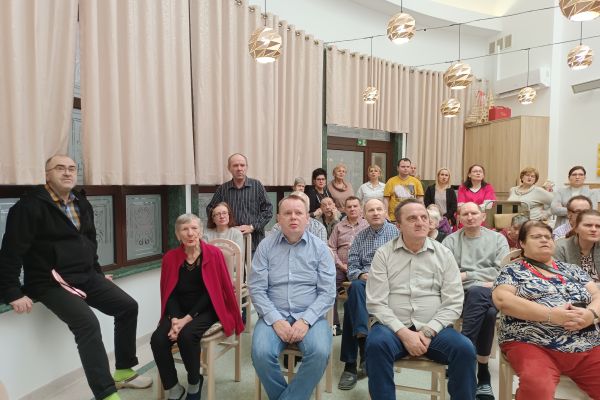 Mieszkańcy na siedząco śpiewaja kolęde.