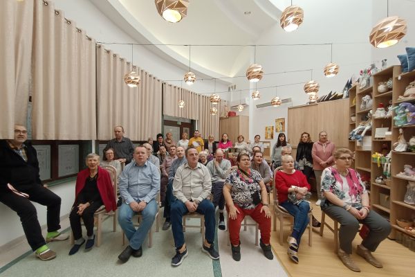 Mieszkańcy na siedząco śpiewaja kolęde.