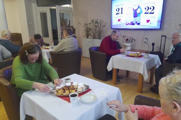 Mieszkańcy siedzą przy stolikach przy poczęstunku.