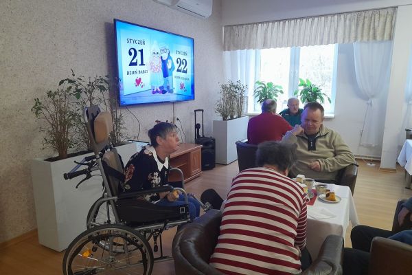 Mieszkańcy siedzą przy stolikach przy poczęstunku.