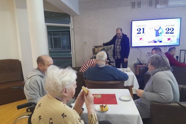 Mieszkańcy siedzą przy stolikach przy poczęstunku.