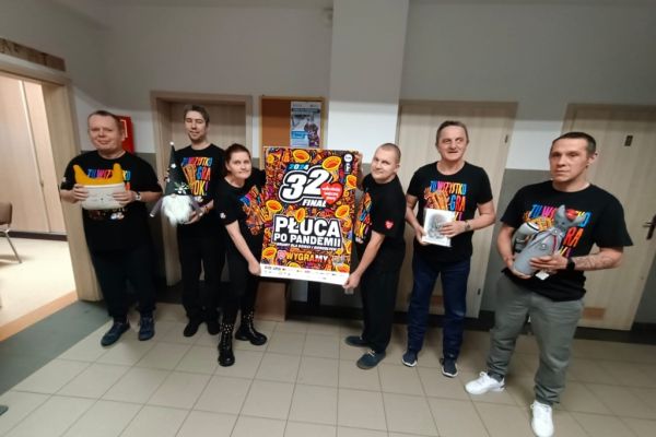 Grupowe zdjęcie mieszkańców w koszulkach WOŚP z gadżetami które przekażą na licytacje WOŚP.