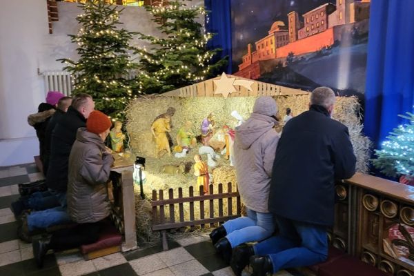 Grupa mieszkańców modli się w kościele klęcząc przy szopce.