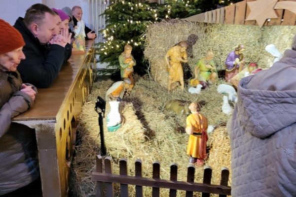 Grupa mieszkańców modli się w kościele klęcząc przy szopce.