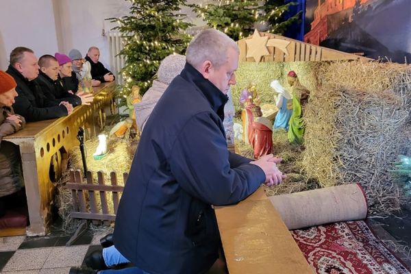 Grupa mieszkańców modli się w kościele klęcząc przy szopce.