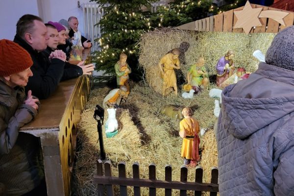 Grupa mieszkańców modli się w kościele klęcząc przy szopce.