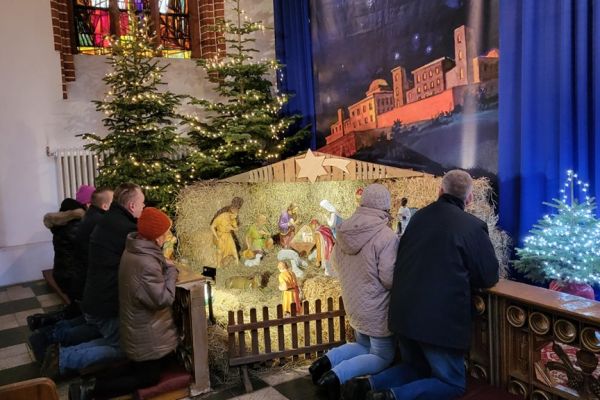 Grupa mieszkańców modli się w kościele klęcząc przy szopce.