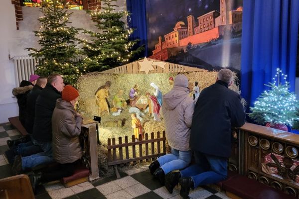 Grupa mieszkańców modli się w kościele klęcząc przy szopce.