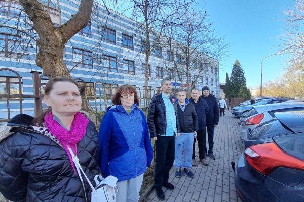 Mieszkańcy stoja przed budynkiem szkoły.