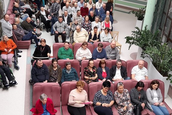 Mieszkańcy na widowni siedzą na krzesłach i fotelach, widok z góry holu Domu z widownią.