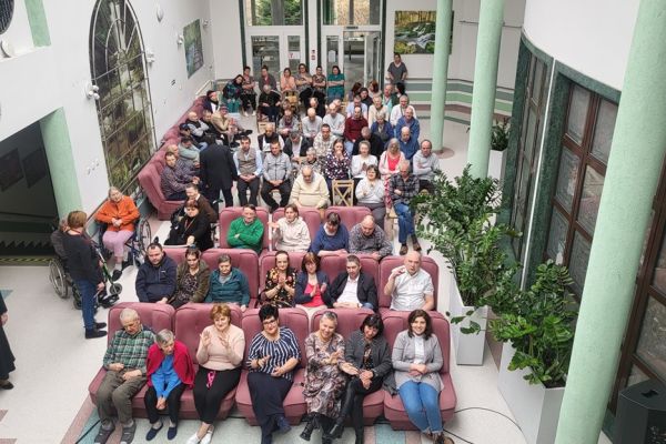 Mieszkańcy na widowni siedzą na krzesłach i fotelach, widok z góry holu Domu z widownią.