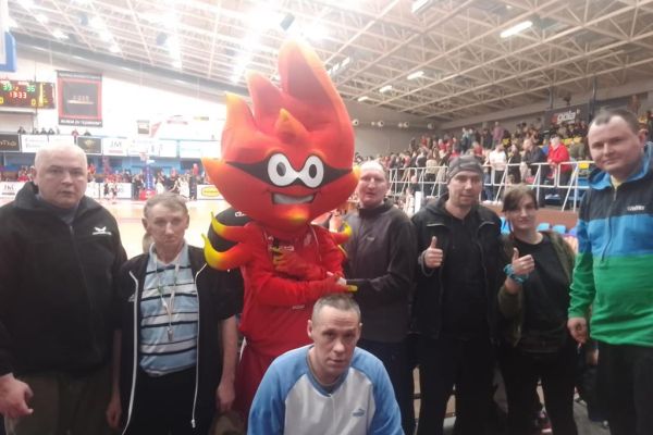 Mieszkańcy stoją na hali Gryfia i pozuja do zdjęcia z maskotką, a w tle widać Boisko halowe.