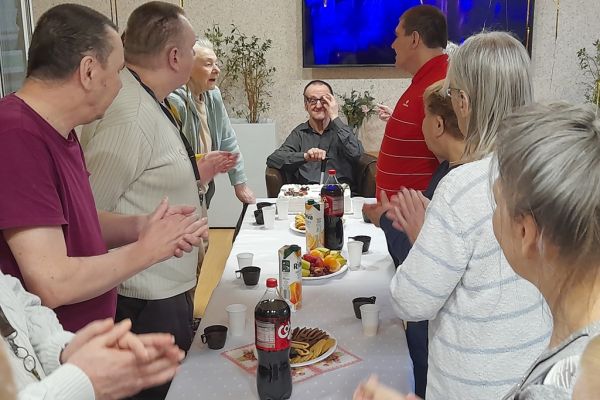 Mieszkańcy na stojąco śpieewają sto lat siedzącemu solenizantowi.