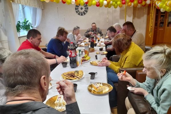 Mieszkańcy siedzą przy długim stole i spożywaja poczęstunek.