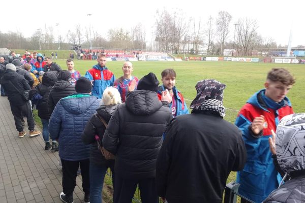Mieszkańcy witają się z zawodnikami przy boisku na meczu piłki nożnej.