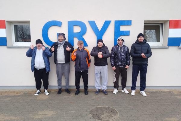 Mieszkańcy stoją przy ścianie z napisem GRYF na meczu piłki nożnej.