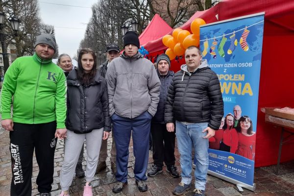 Mieszkańcy stoja przy banerze święta osób z zespołem downa.
