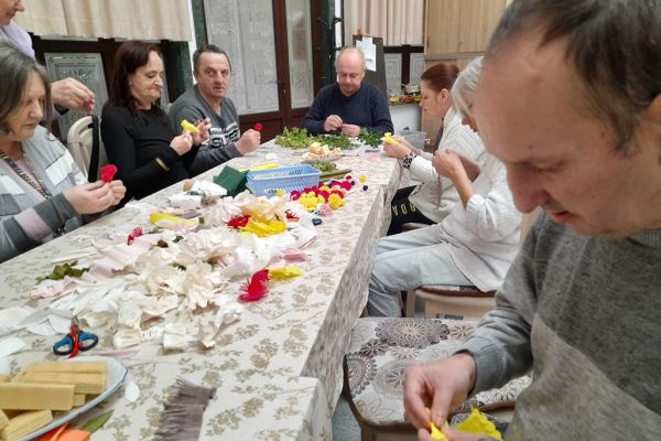 Mieszkańcy wspólnie przy długim stole wykonują palemki.