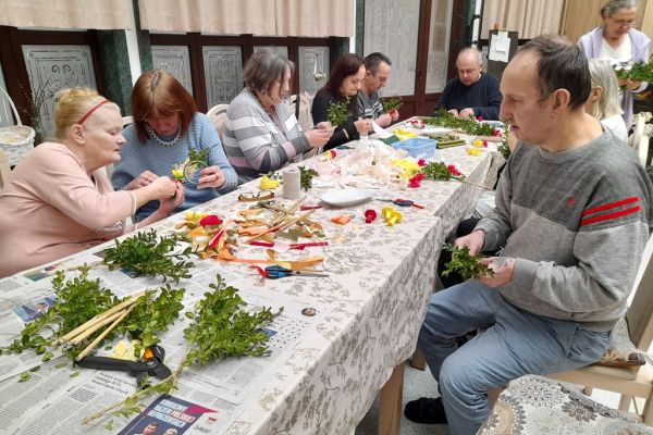 Mieszkańcy wspólnie przy długim stole wykonują palemki.