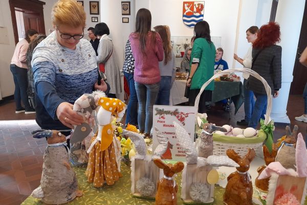 Prace mieszkańców wykonane na terapii zajęciowej na wystawie w Starostwie Powiatowym w Słupsku.Kilka osób ogląda wystawę.