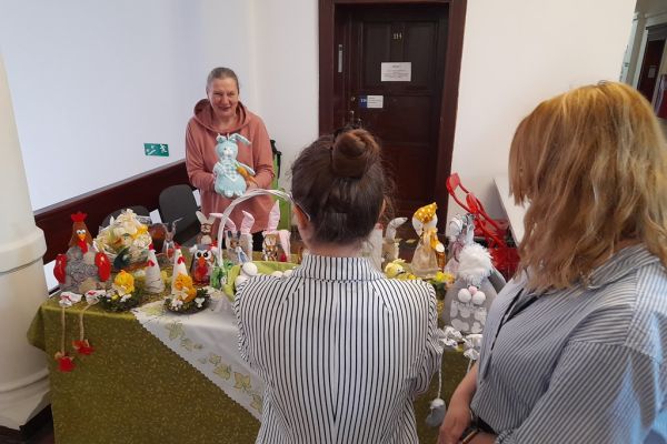 Prace mieszkańców wykonane na terapii zajęciowej na wystawie w Starostwie Powiatowym w Słupsku. Dwie panie oglądają wystawę.