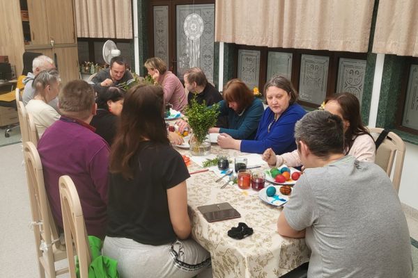Kilkunastu Mieszkańców maluje jajka przy długim stole w sali terapii.