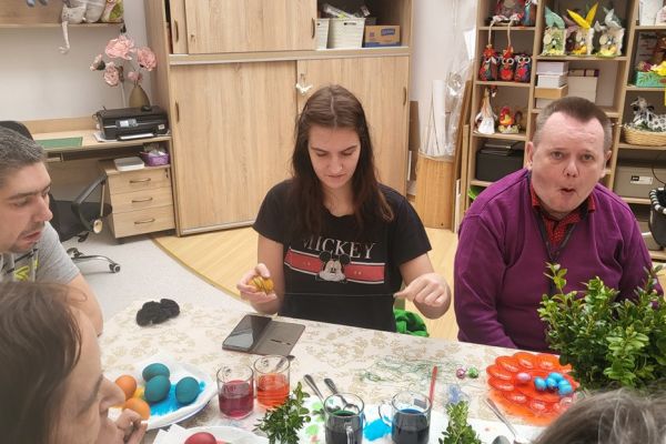 Troje Mieszkańców maluje jajka przy długim stole w sali terapii.