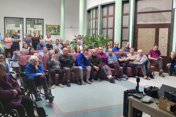 Mieszkańcy siedzą w rzędach foteli i krzeseł ustawionych na holu i oglądają film z projektora. 